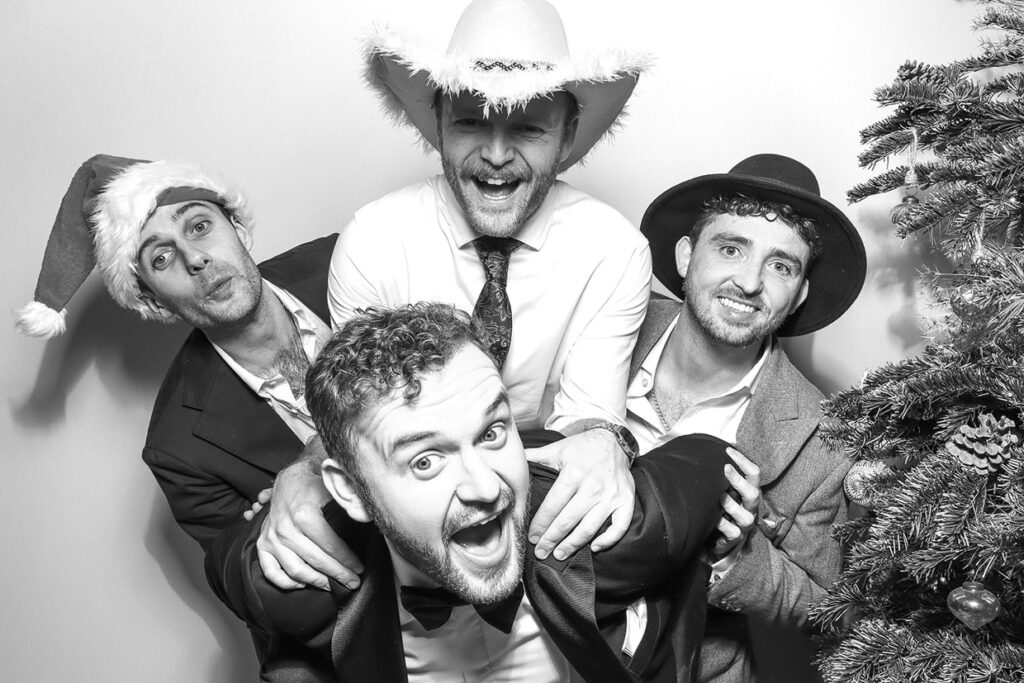 black and white print of 4 guests posing near a christmas tree, during a christmas photo booth event in the cotswolds