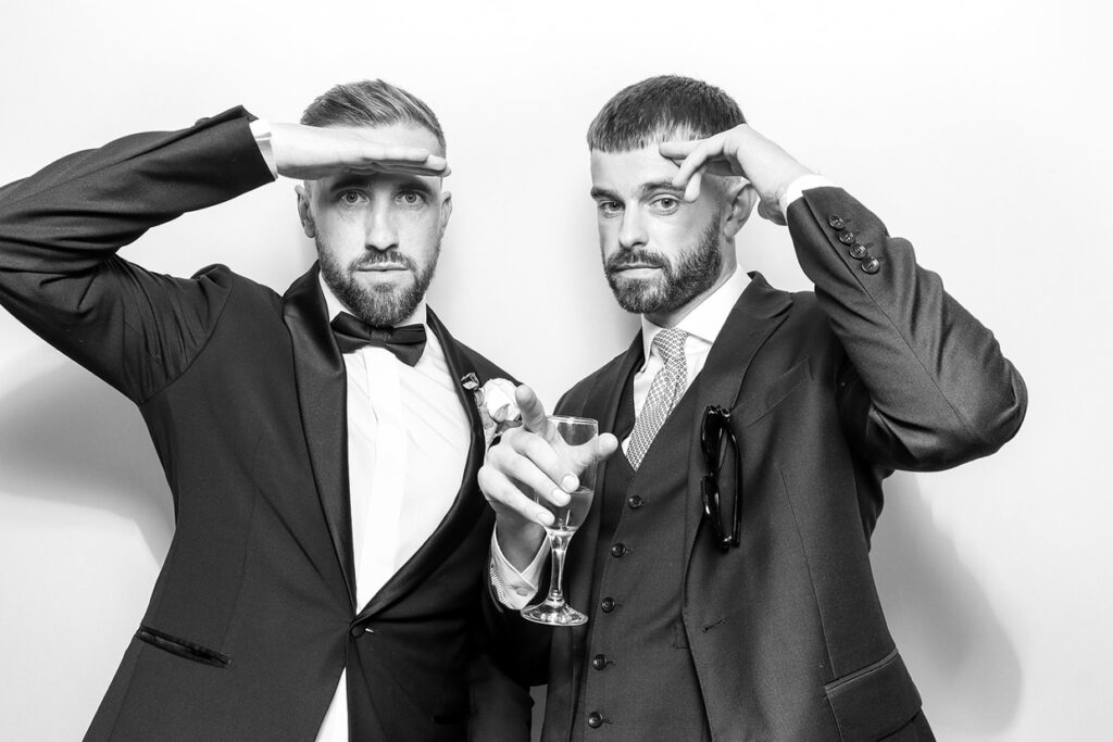 black and white photography of 2 guests posing against a white 
 background, during a christmas party entertainment with an Affordable Christmas Photo Booth Rental for weddings and corporate parties