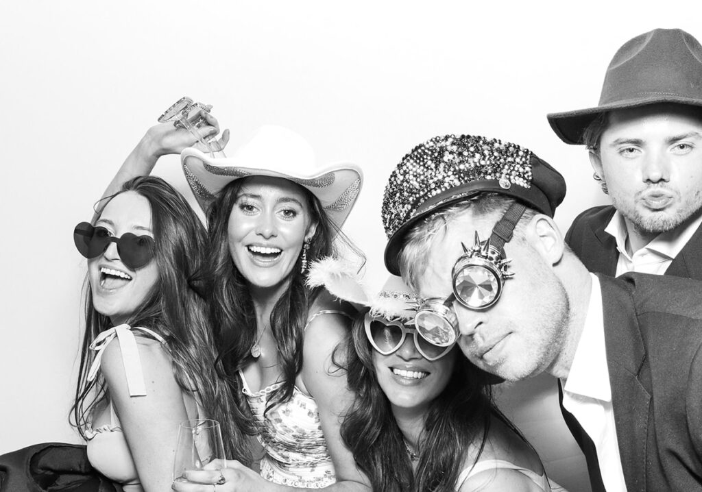 black and white photography of 5 guests posing against a white 
 background, during a christmas party entertainment with an Affordable Christmas Photo Booth Rental for weddings and corporate parties