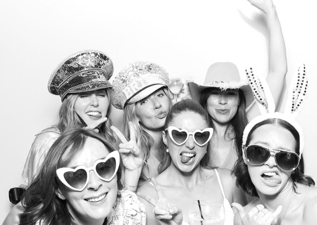 black and white print of large group of guests posing against a white 
 background, during a private party event with an Affordable Christmas Photo Booth Rental for weddings and corporate parties