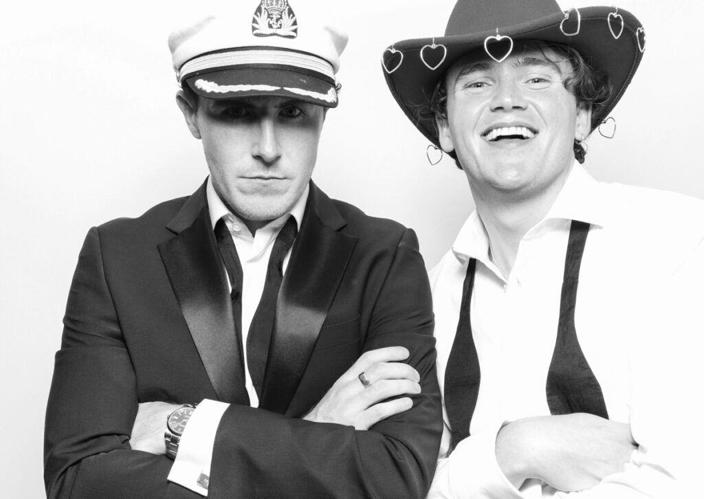 2 guests posing against a white backdrop, using the b&w filter during a corporate event party entertainment, with mad hat photo booth hire