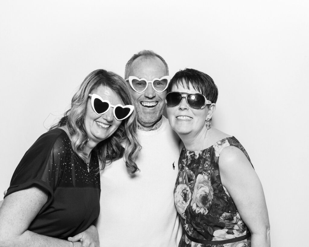 b&w photo of 3 guests posing with sunglasses and props for best wedding party entertainment during a reception event at Banbury barn in Oxfordshire, with mad hat photo booth rental