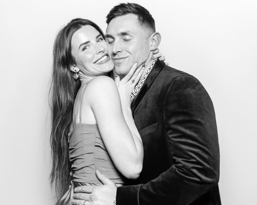 b&w photo of a couple posing against a white backdrop during a wedding reception entertainment party with mad hat photo booth in a Banbury wedding venue, Oxfordshire