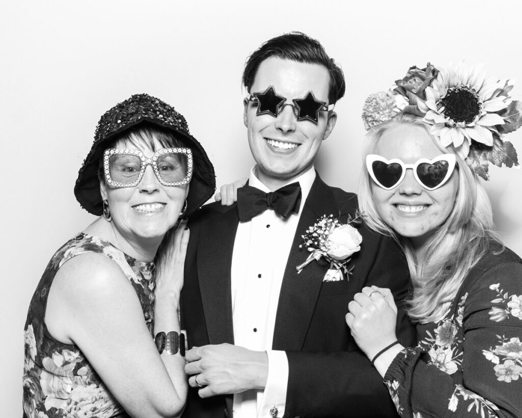 b&w photo of 3 guests posing with sunglasses and props for best wedding party entertainment during a reception event at Banbury barn in Oxfordshire, with mad hat photo booth rental