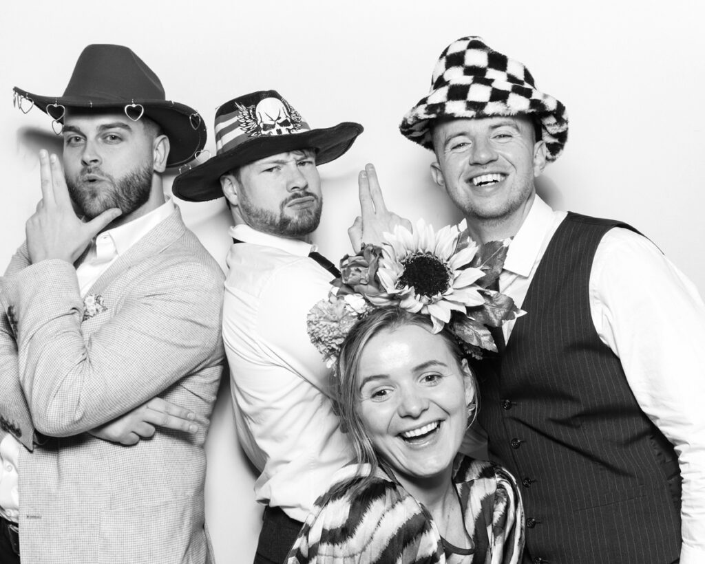 b&w photo of 4 guests posing and having fun with sequins hats and props during a wedding party entertainment with  mad hat photo booth rental in Banbury