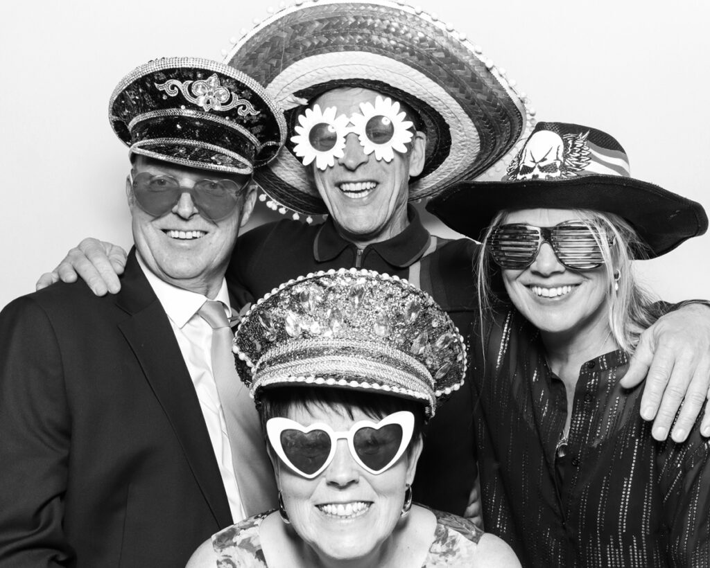 b&w photo of 4 guests posing and having fun with sequins hats and props during a wedding party entertainment with  mad hat photo booth rental in Banbury