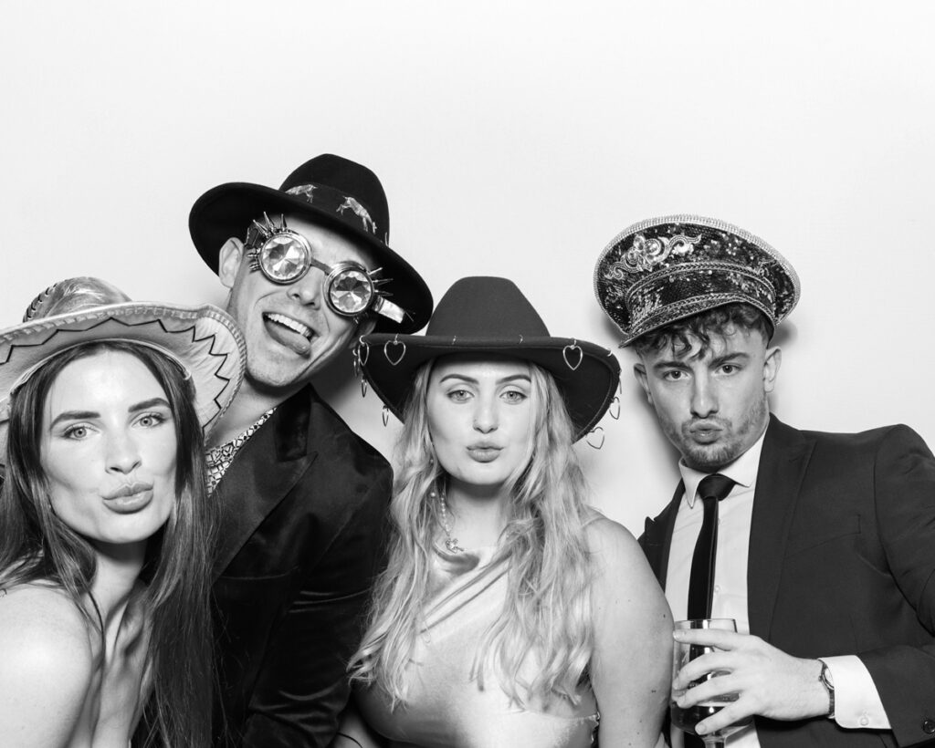 b&w photo of 4 guests posing and having fun with sequins hats and props during a wedding party entertainment with  mad hat photo booth rental in Banbury