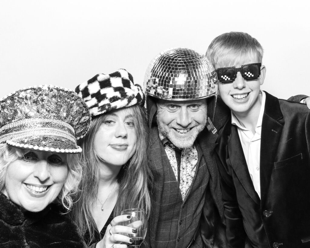 b&w photo of 4 guests posing and having fun with sequins hats and props during a wedding party entertainment with  mad hat photo booth rental in Banbury