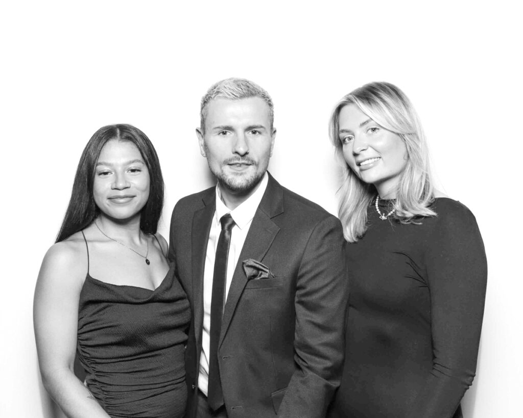 Black and white group photo of three individuals dressed in formal evening attire, smiling at a Cheltenham Racecourse corporate celebration