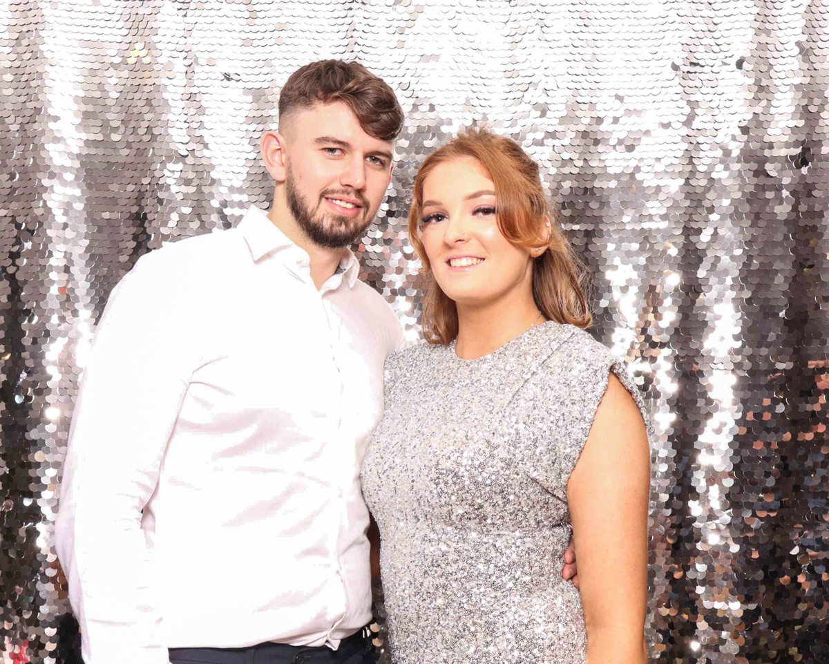 A group of 2 guests dressed formally, posing against a silver sequins backdrop, for a photo booth for a corporate event.