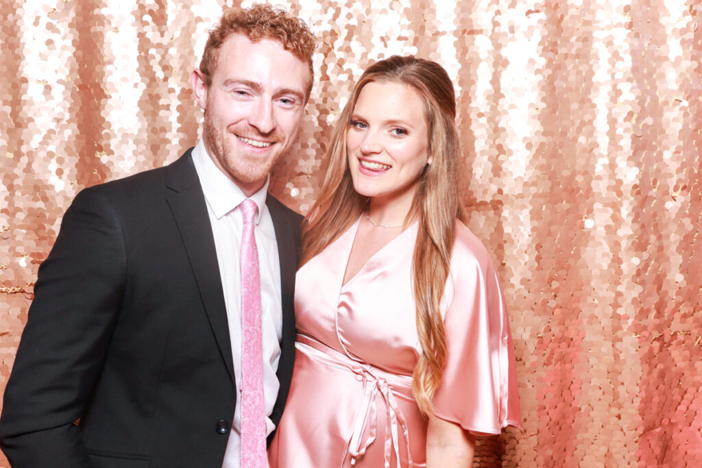 A couple dressed in formal attire, with a rose gold sequin backdrop highlighting sophisticated photo booth options for corporate events.