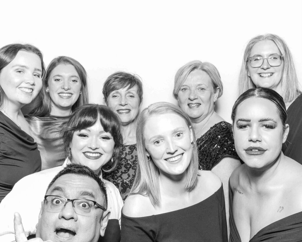 black and white image of A group of colleagues gathered closely, smiling and enjoying a fun photo booth session at a corporate event, creating lasting memories at cheltenham race course