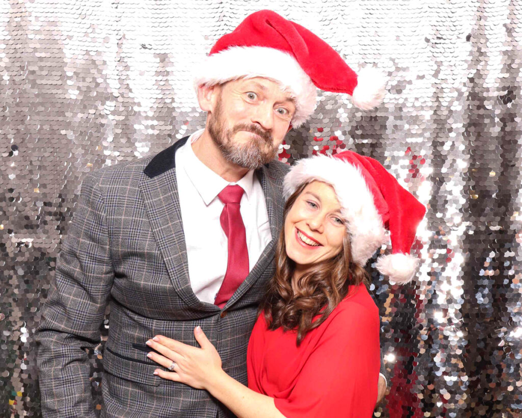 Guests at a Christmas staff party wearing Santa hats and posing against a silver sequins backdrop