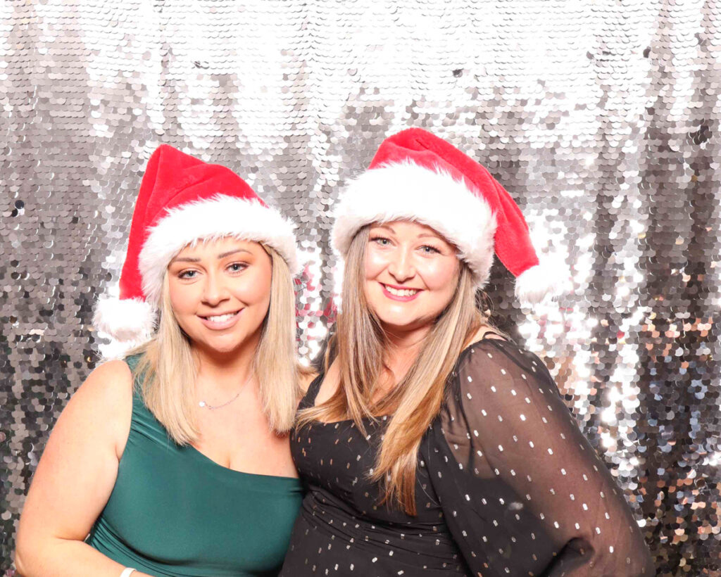 Two women smiling in Santa hats, enjoying the festive photo booth at a Christmas staff party