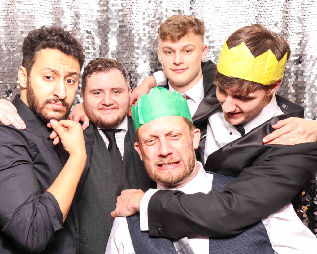 A group of colleagues sharing a funny moment with festive paper crowns at a Christmas staff party photo booth