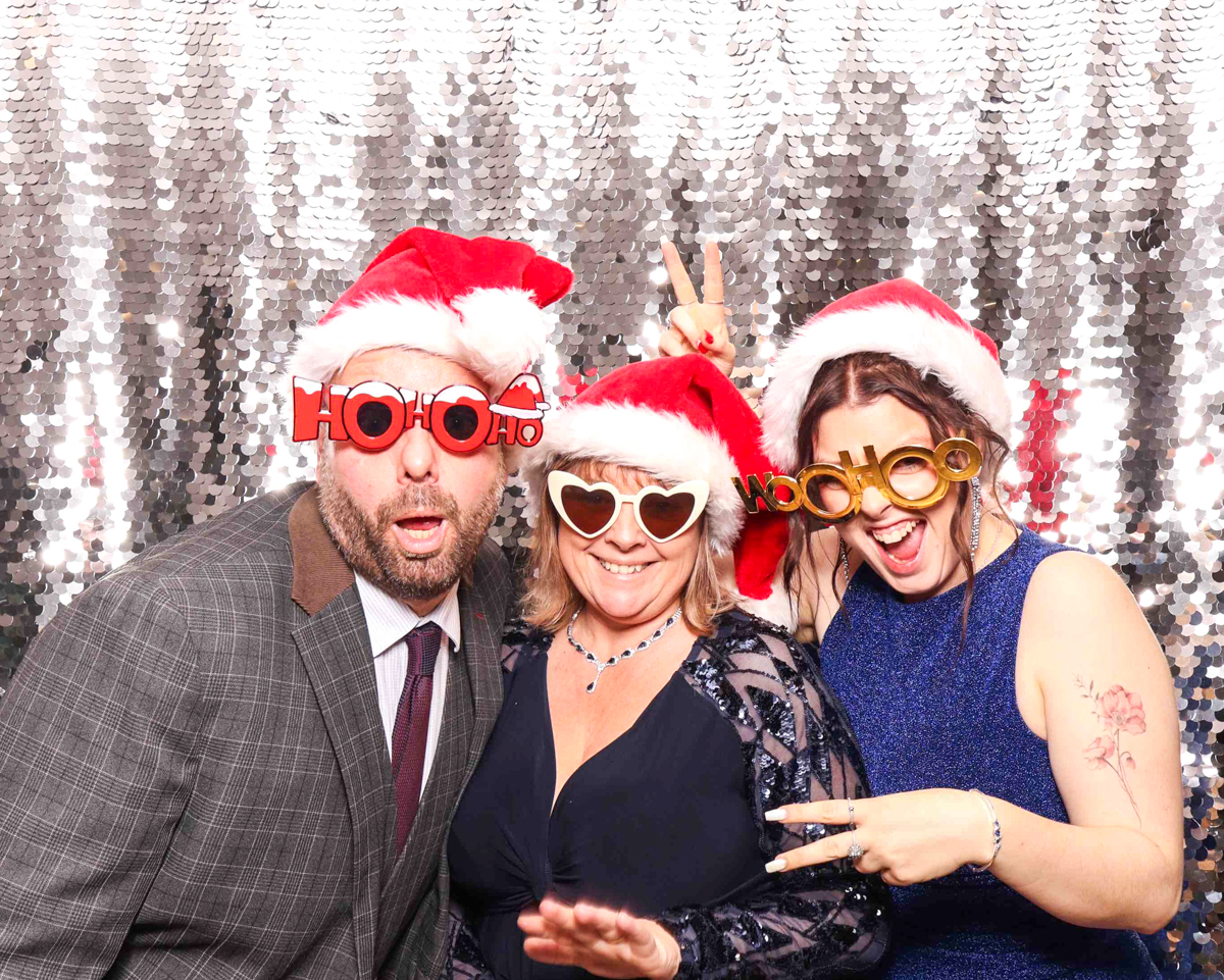 A lively group of colleagues celebrating with festive props, hats, and a silver sequins photo booth backdrop