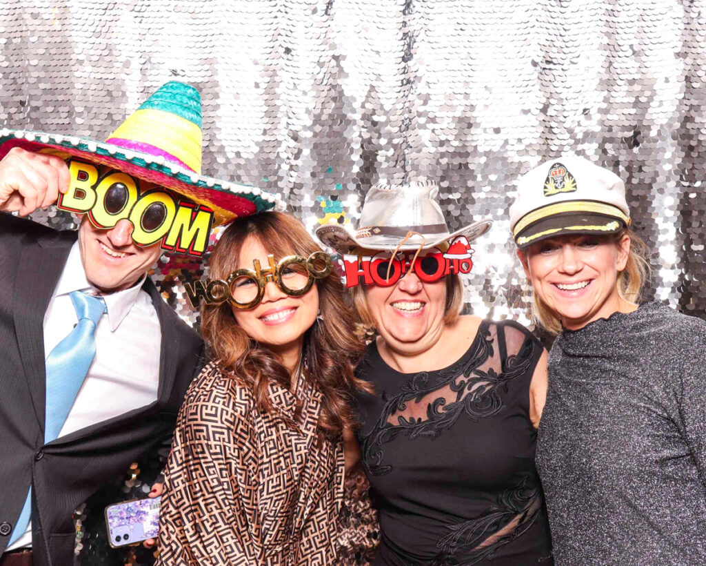 Party guests wearing themed props, including cowboy hats and holiday glasses, at a Christmas staff party photo booth