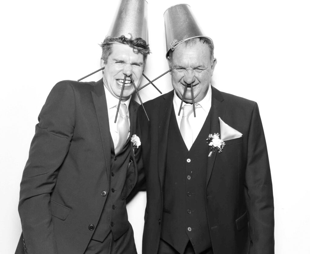 Guests in the Cripps Barn photo booth having a laugh, styled with bucket hats and creative straw props, perfectly capturing the playful atmosphere.