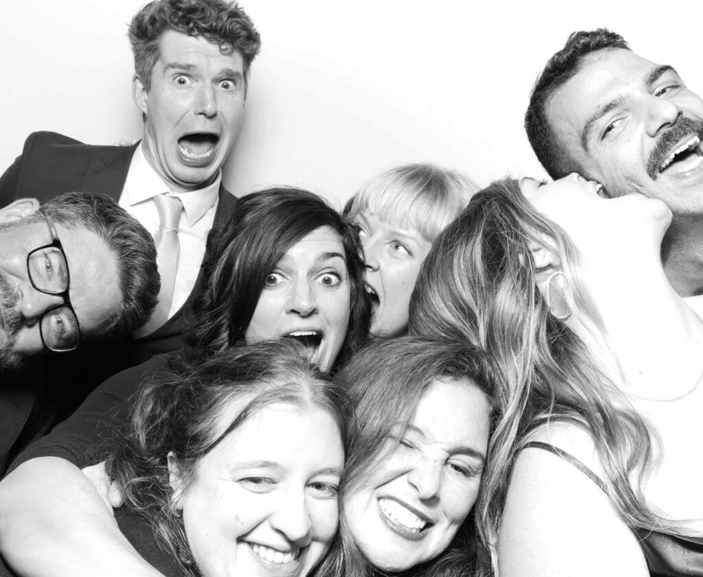 A humorous Cripps Barn photo booth shot featuring friends in a close embrace, each displaying funny and surprised expressions.