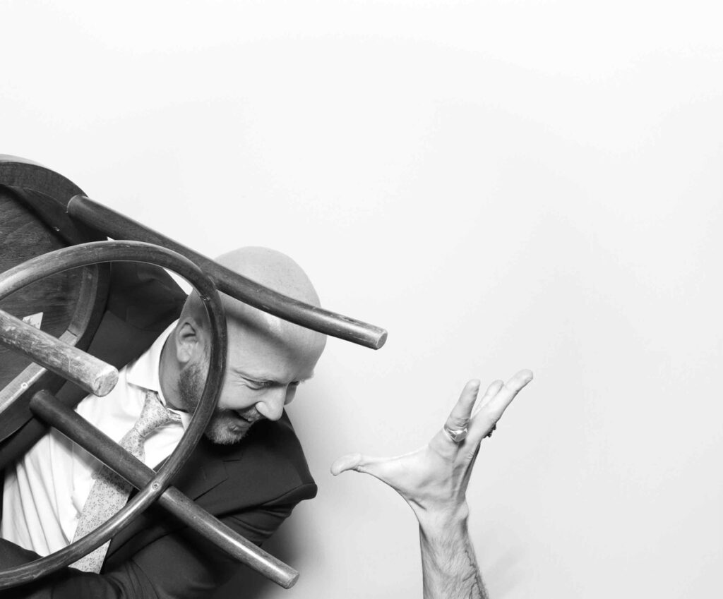 A black-and-white photo of two wedding guests mid-action in a dramatic and comedic chair-related pose against a white backdrop during a cripps barn wedding