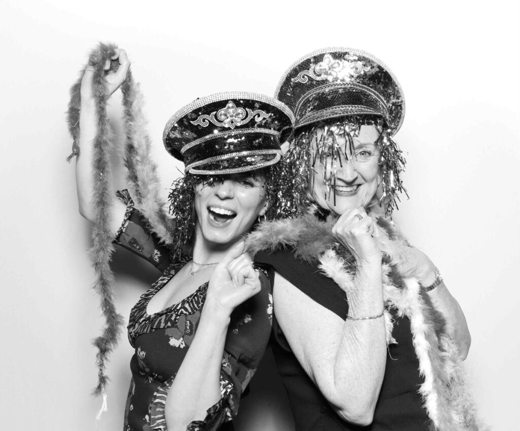 Two guests at Cripps Barn posing in a photo booth, both wearing sequinned hats with tinsel wigs and giving peace signs, radiating joy and laughter.