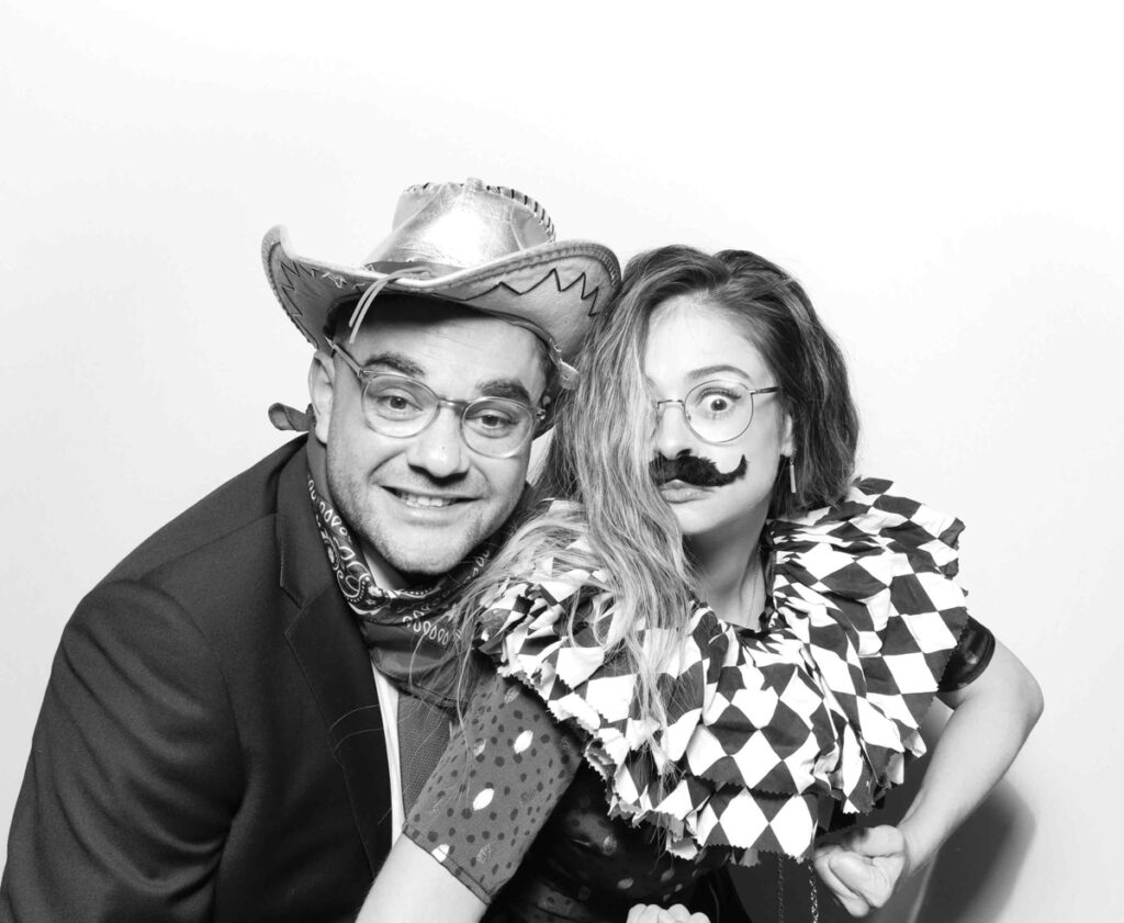 Guests striking a dramatic and fun pose in a photo booth, one with outstretched arms and the other with a confident stance.