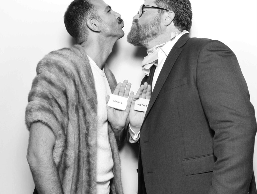 Two guests in a humorous photo booth pose, one wearing a fur stole and the other in a suit holding a name tag during a cripps barn photo booth party entertainment