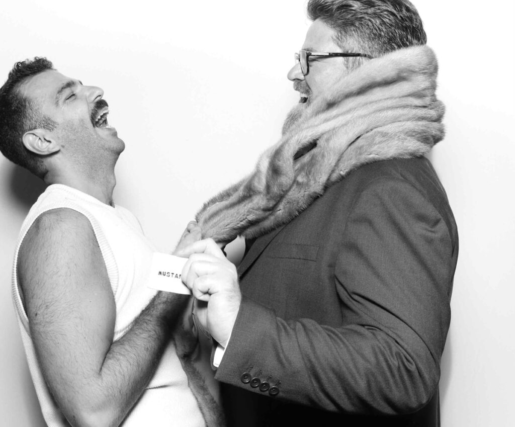 Two guests laughing and interacting with a fur stole in the photo booth, capturing the fun and spontaneous vibe of the event party entertainment at cripps barn wedding venue cotswolds