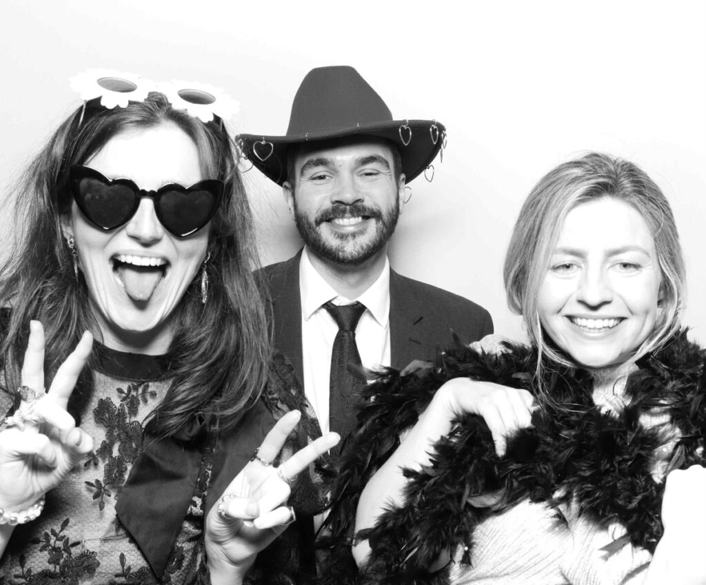 A playful photo booth scene at Cripps Barn with guests wearing sequinned hats, a disco helmet, and making peace signs while expressing their fun personalities.