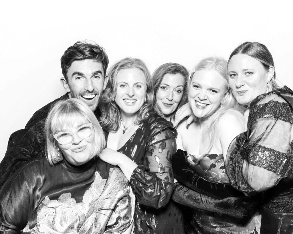 Smiling group of guests dressed in elegant attire posing for a black and white photo in a professional photo booth at an Oxfordshire corporate or wedding event