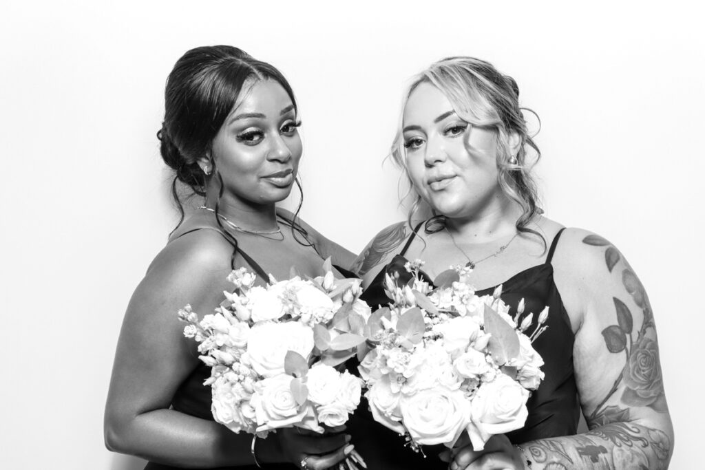 Two bridesmaids holding bouquets of flowers, posing elegantly in a black and white photo booth session at a wedding event entertainment