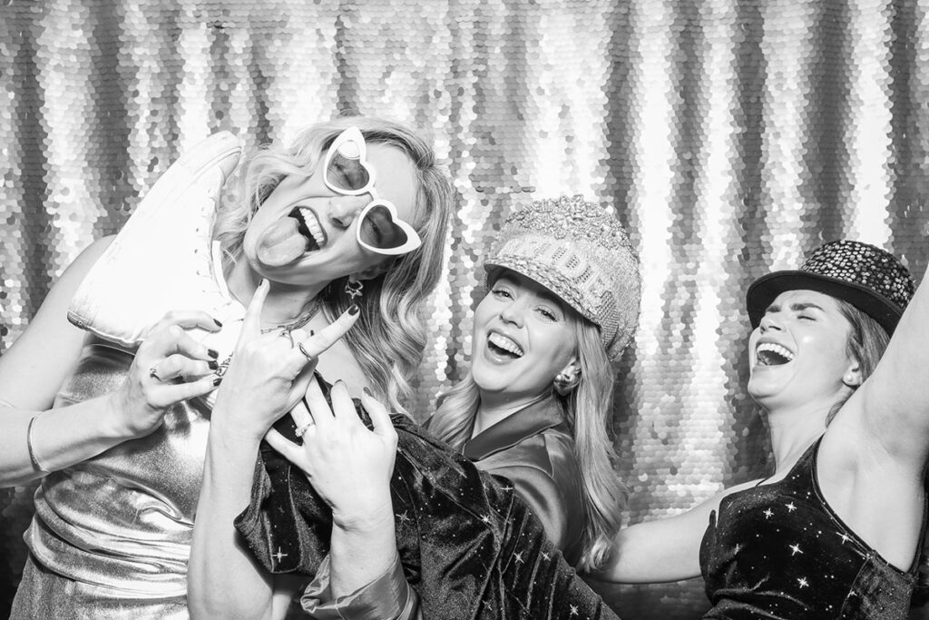 black and white image of couple using a christmas photo booth with guests using a silver sequins backdrop and christmassy props