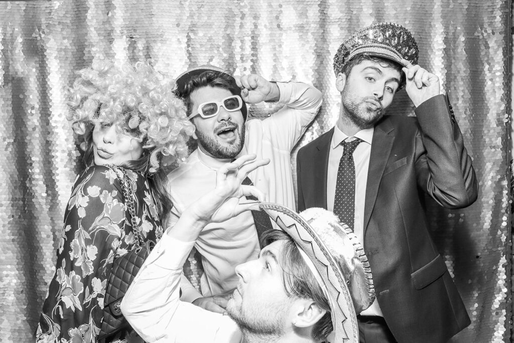 black and white image of couple using a christmas photo booth with guests using a silver sequins backdrop and christmassy props