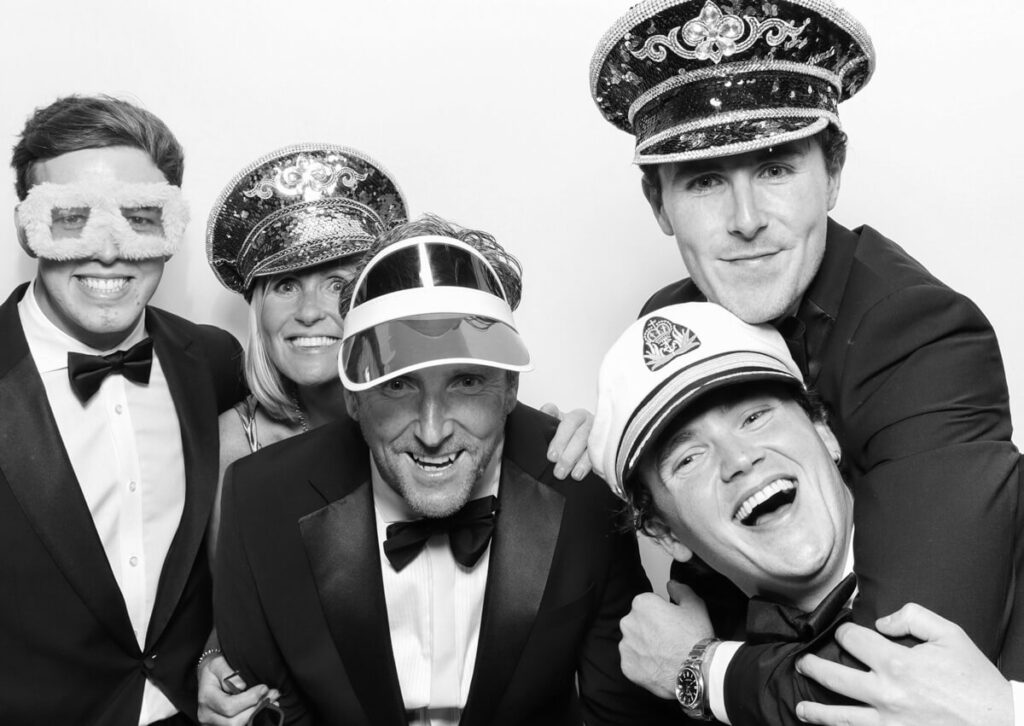 group of 5 people posing wearing props against a white backdrop for a luxury wedding photo booth rental at Kin House