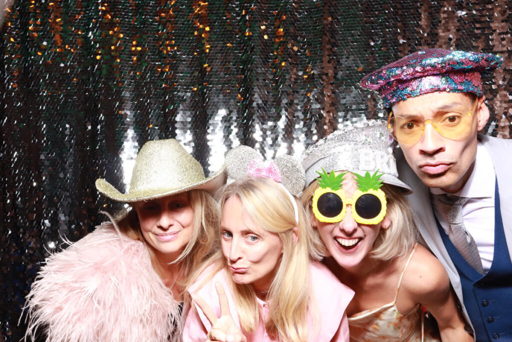 guests during a party entertainment evening, posing with fun props, against a silver sequins backdrop, for a party entertainment hire and rental in bristol