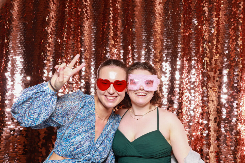 2 guests posing while wearing fun party sunglasses, against a champagne sequins backdrop, for a birthday party entertainment hire in Cotswolds area