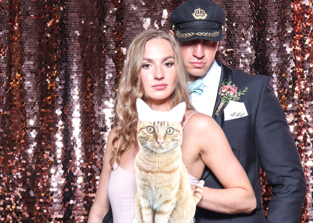 2 guests posing with a cat cut out, against a champagne sequins backdrop, for a cripps barn cotswolds wedding party entertainment with mad hat photo booth hire for parties, birthdays and weddings