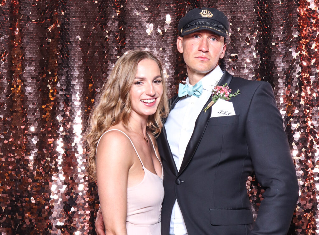 2 guests posing with super fun props, against a champagne sequins backdrop, for a cripps barn cotswolds wedding party entertainment with mad hat photo booth hire for parties, birthdays and weddings