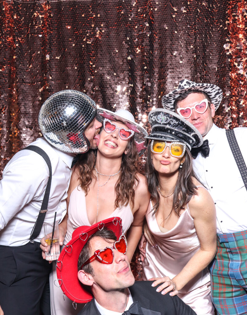 large group of guests posing with super fun props, against a champagne sequins backdrop, for a cripps barn cotswolds wedding party entertainment with mad hat photo booth hire for parties, birthdays and weddings