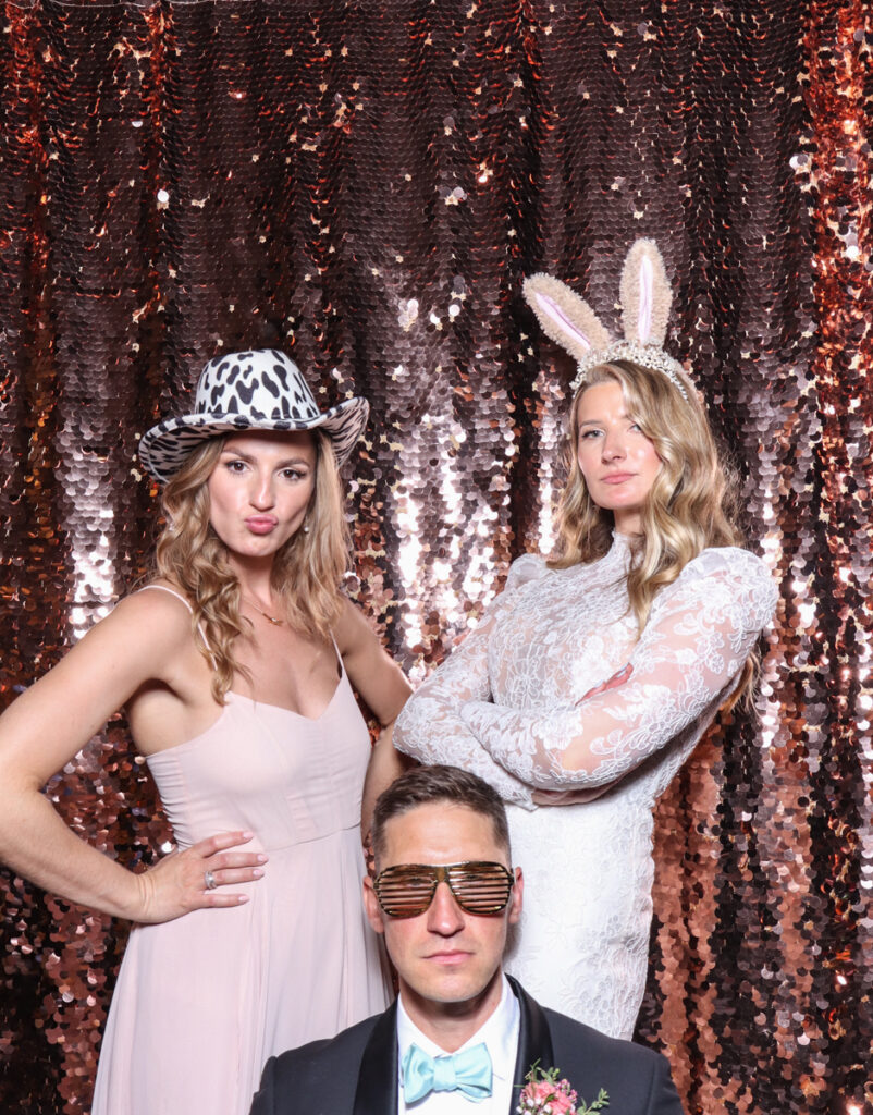 3 guests, including the bride, posing with super fun props, against a champagne sequins backdrop, for a cripps barn cotswolds wedding party entertainment with mad hat photo booth hire for parties, birthdays and weddings