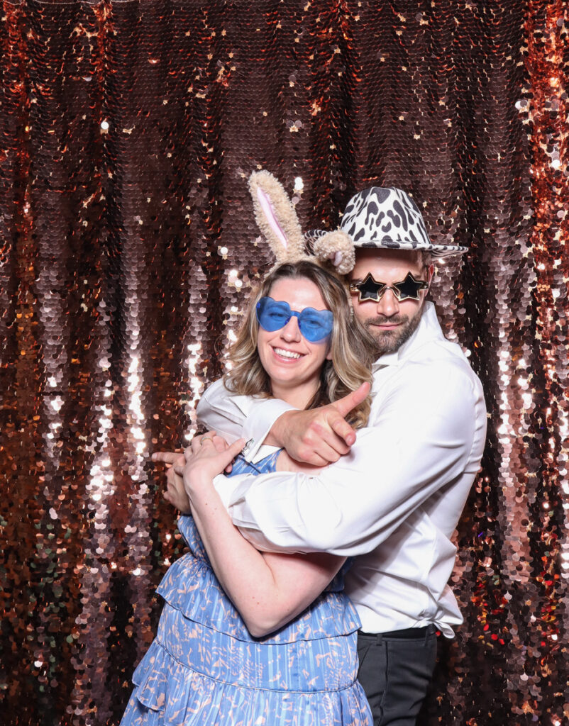 2 guests posing with super fun party props, against a champagne sequins backdrop, for a cripps barn cotswolds wedding party entertainment with mad hat photo booth hire for parties, birthdays and weddings