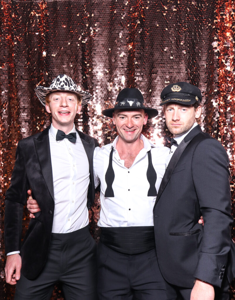 3 guests posing against a champagne sequins backdrop , during a wedding party in the cotswolds