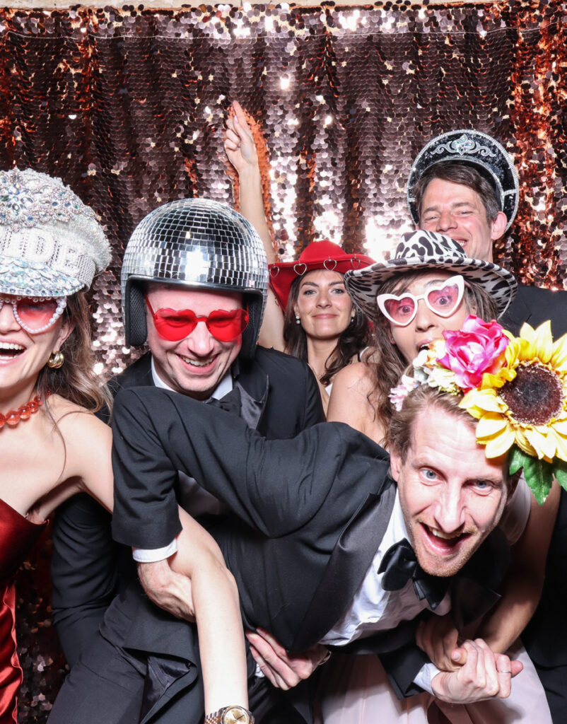 large group of guests posing with super fun props, against a champagne sequins backdrop, for a cotswolds wedding party entertainment with mad hat photo booth hire for parties, birthdays and weddings
