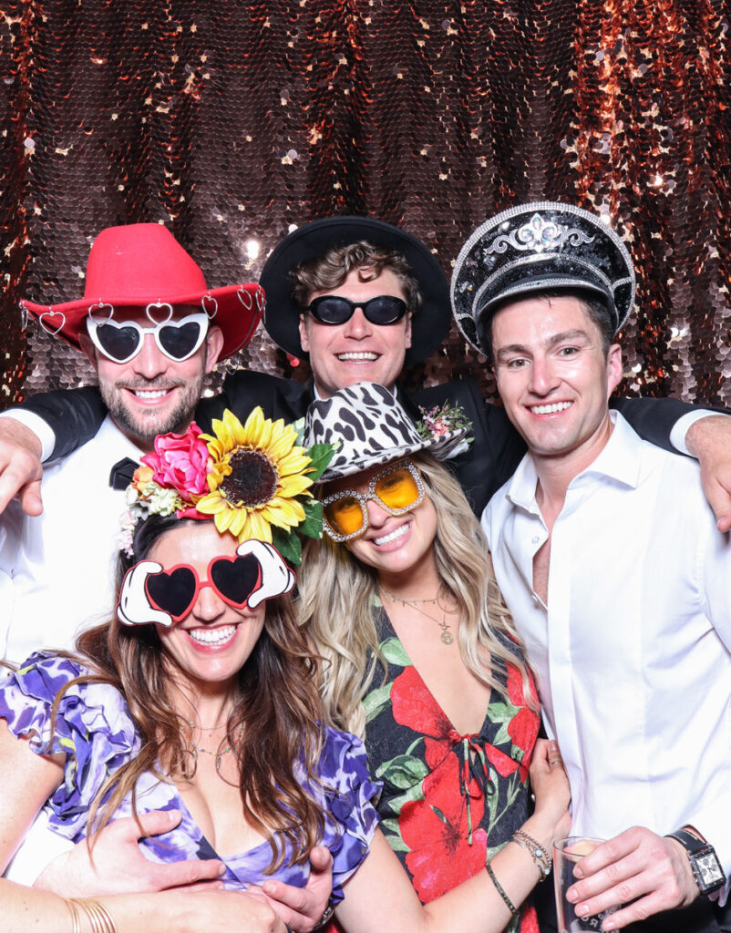 large group of guests posing with super fun props, against a champagne sequins backdrop, for a cripps barn cotswolds wedding party entertainment with mad hat photo booth hire for parties, birthdays and weddings