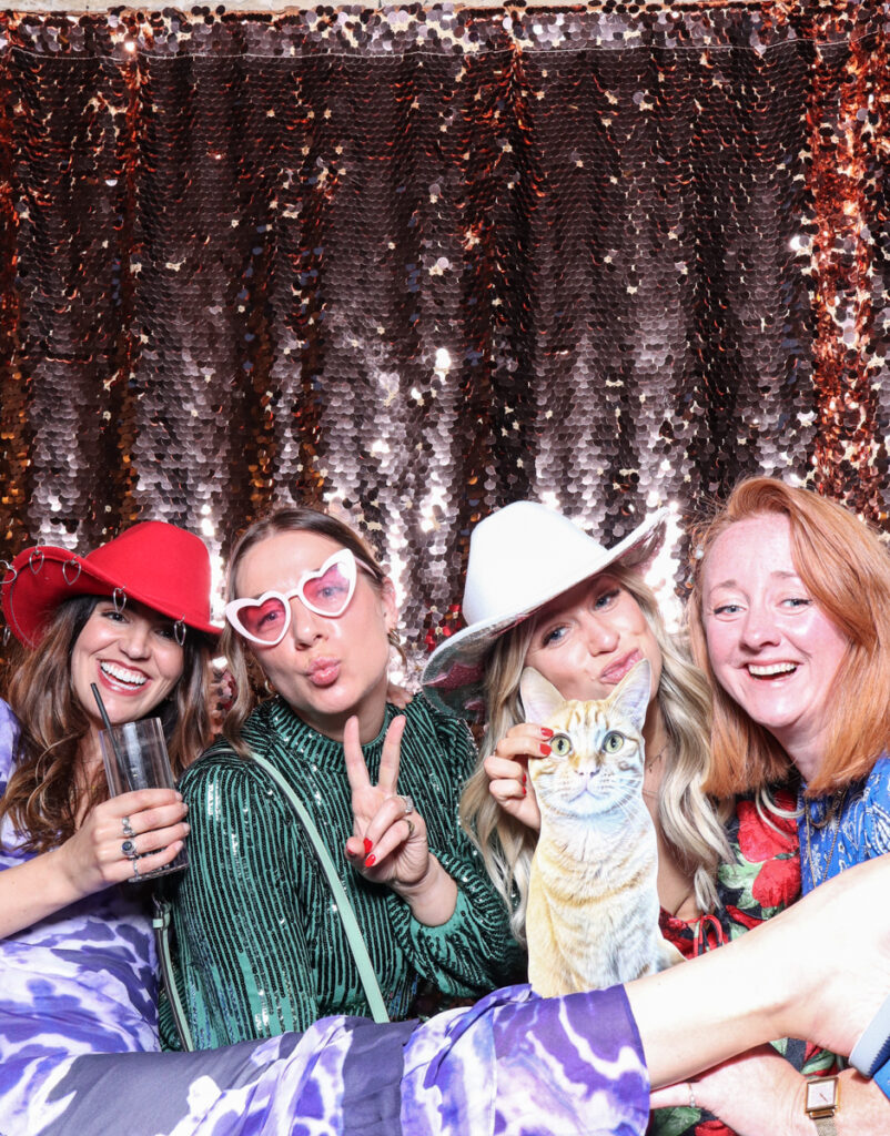 large group of guests posing with super fun props, against a champagne sequins backdrop, for a cotswolds wedding party entertainment with mad hat photo booth hire for parties, birthdays and weddings