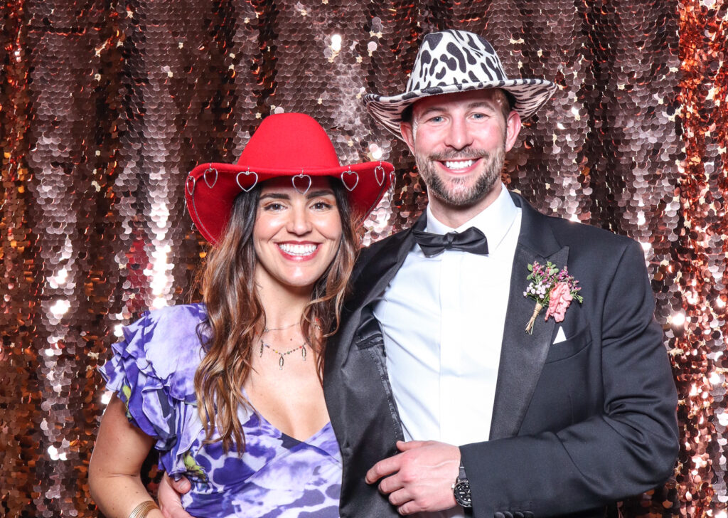 2 guests posing with super fun props, against a champagne sequins backdrop, for a cripps barn cotswolds wedding party entertainment with mad hat photo booth hire for parties, birthdays and weddings