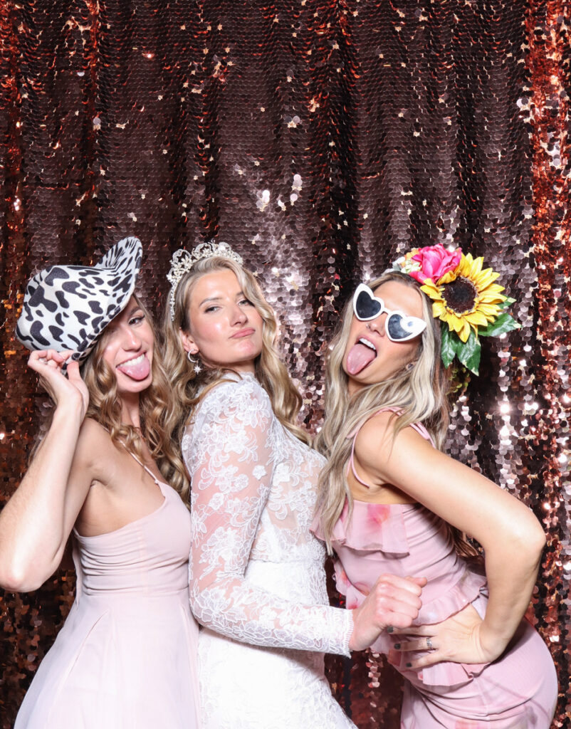 3 guests posing with super fun props, against a champagne sequins backdrop, for a cripps barn cotswolds wedding party entertainment with mad hat photo booth hire for parties, birthdays and weddings