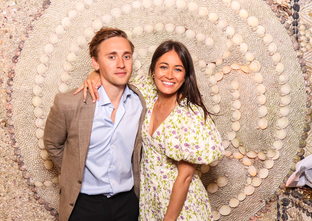 Couple dressed smartly, smiling against a backdrop of cream-toned shells arranged in a spiral design.
