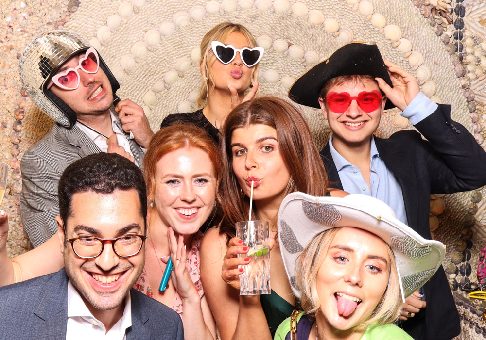Lively group of guests dressed for a party, with heart glasses, pirate hats and a disco helmet, enjoying the booth together at Belcombe Court