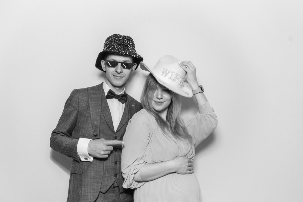 Wedding couple playfully pointing at each other while wearing fun hats, including one with the word “WIFE” in sparkles.